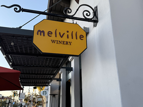 Yellow sign reading "melville WINERY" on a building exterior.