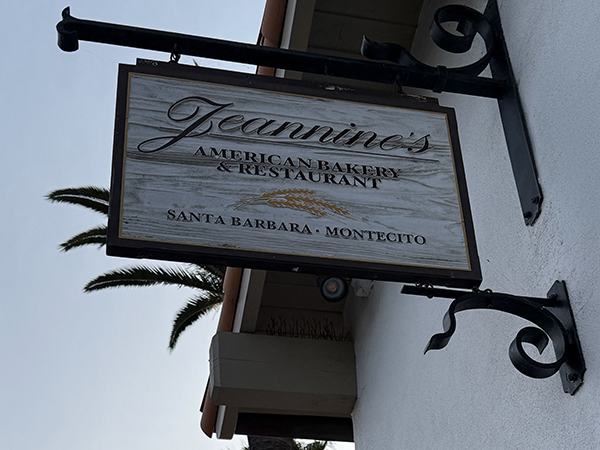 A wooden sign for "Jeannine's American Bakery & Restaurant" is mounted on a building, with palm trees visible in the background.