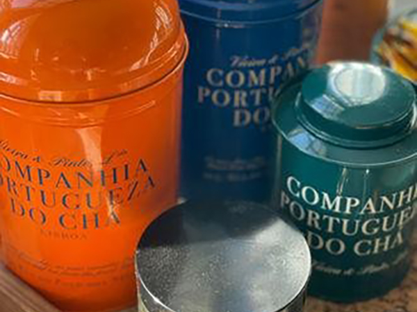 Colorful tea tins with "Companhia Portugueza do Chá" branding, featuring orange, blue, and green containers, are displayed on a surface.