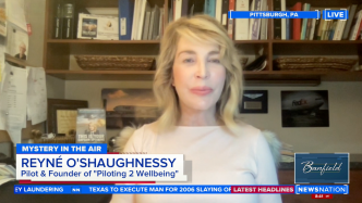 A woman identified as Reyné O'Shaughnessy appears on a video call interview with news graphics displaying her title and location in a home office setting.